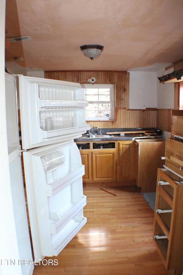 kitchen with refrigerator, wooden walls, sink, and light hardwood / wood-style floors