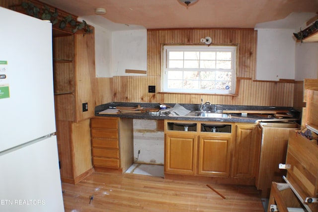 kitchen featuring wooden walls, sink, white fridge, and light wood-type flooring