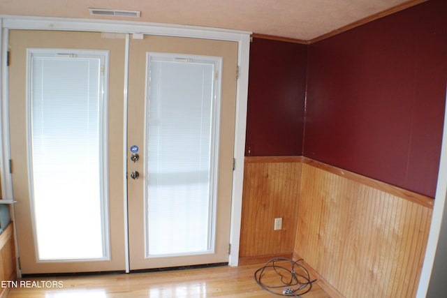 doorway featuring ornamental molding, wood walls, light wood-type flooring, and french doors