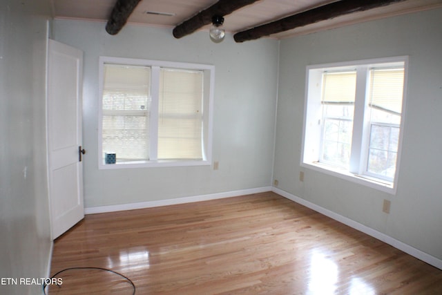 spare room with beamed ceiling, a healthy amount of sunlight, and light wood-type flooring