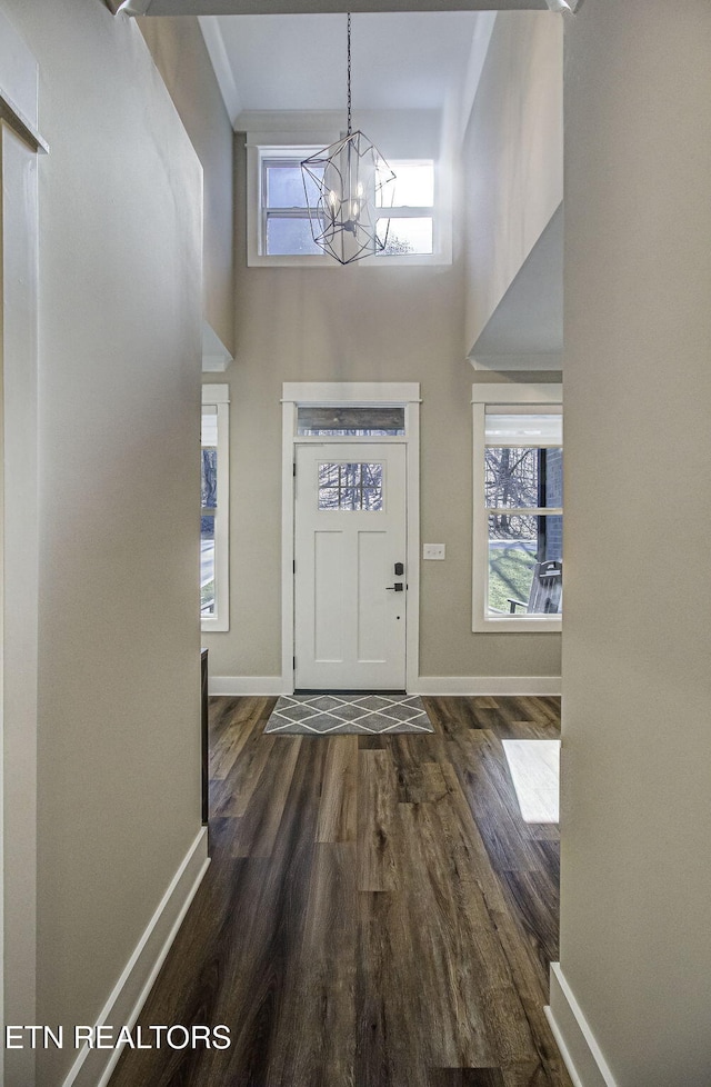 entrance foyer featuring a towering ceiling, a notable chandelier, plenty of natural light, and dark wood-style flooring