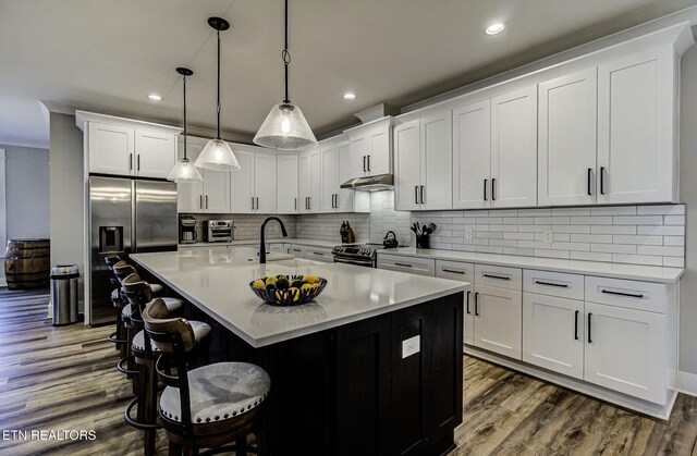 kitchen with stainless steel appliances, dark wood-style flooring, a sink, and a kitchen island with sink