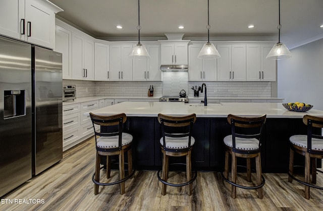 kitchen with appliances with stainless steel finishes, dark wood-style flooring, light countertops, under cabinet range hood, and white cabinetry