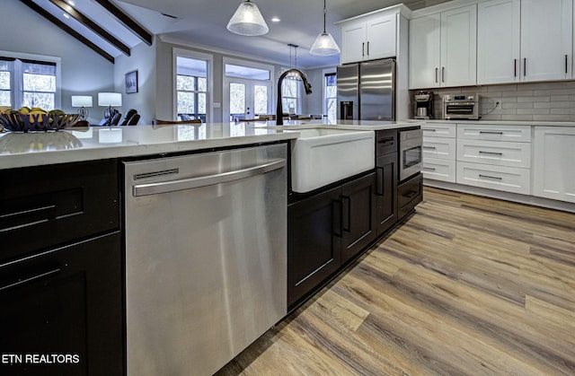 kitchen with light wood finished floors, white cabinets, appliances with stainless steel finishes, vaulted ceiling with beams, and a sink