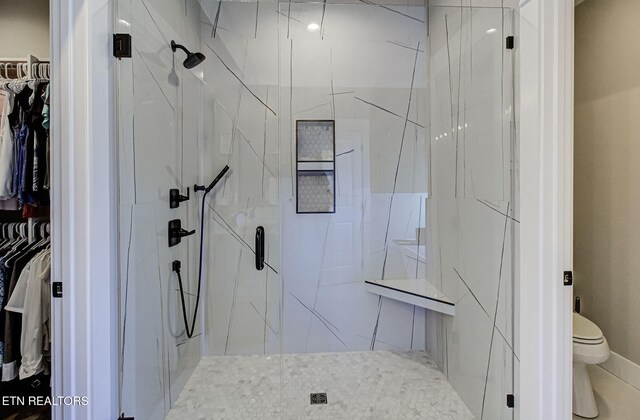 full bathroom featuring a walk in closet, toilet, and a marble finish shower