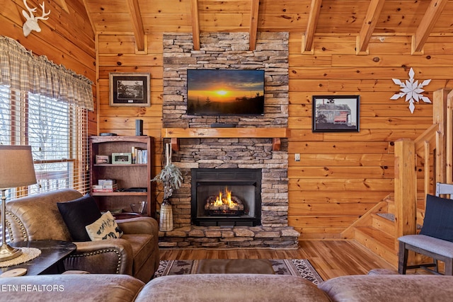 living room featuring a stone fireplace, vaulted ceiling with beams, wood ceiling, wooden walls, and hardwood / wood-style flooring