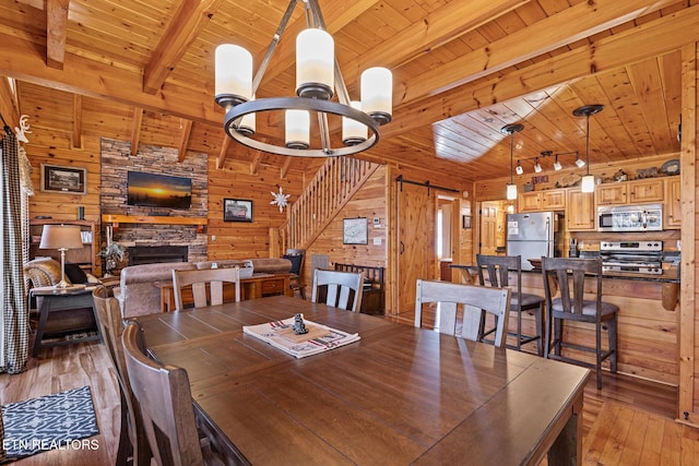 dining room featuring wood ceiling, a stone fireplace, a barn door, beamed ceiling, and wood walls