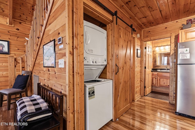 laundry room with wood walls, wood ceiling, a barn door, and stacked washing maching and dryer