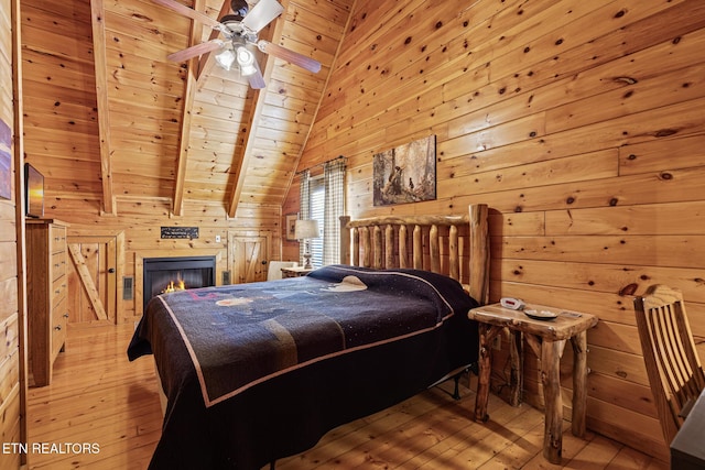 bedroom with wood walls, vaulted ceiling with beams, wooden ceiling, ceiling fan, and light hardwood / wood-style floors