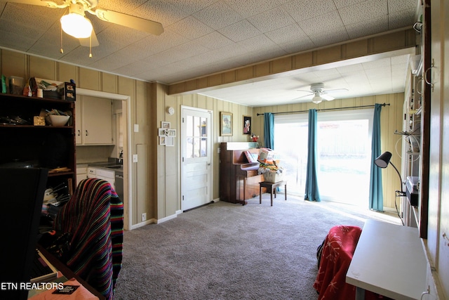 carpeted living room featuring ceiling fan, sink, and wood walls