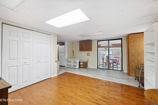 basement featuring fridge, a drop ceiling, and light wood-type flooring