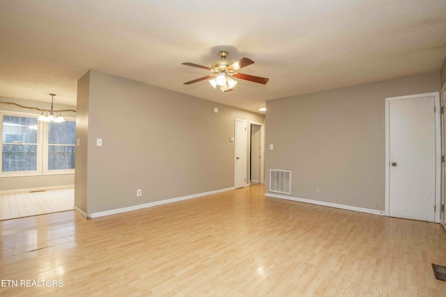 empty room with ceiling fan with notable chandelier, light hardwood / wood-style floors, and a textured ceiling