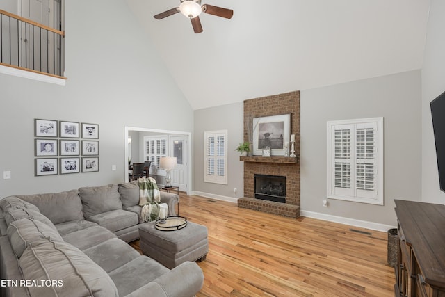 living room with light wood-type flooring, ceiling fan, a fireplace, and high vaulted ceiling