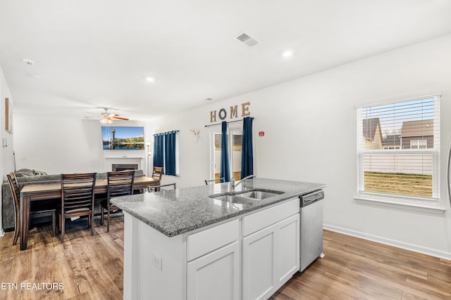 kitchen with white cabinets, dishwasher, sink, a center island with sink, and stone counters