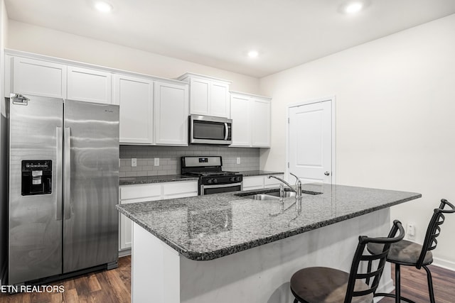 kitchen featuring appliances with stainless steel finishes, sink, white cabinets, dark wood-type flooring, and an island with sink