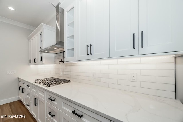 kitchen featuring wall chimney range hood, white cabinetry, light stone counters, and stainless steel gas cooktop