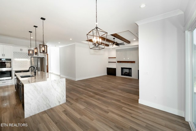 kitchen with pendant lighting, appliances with stainless steel finishes, sink, ornamental molding, and a kitchen island with sink