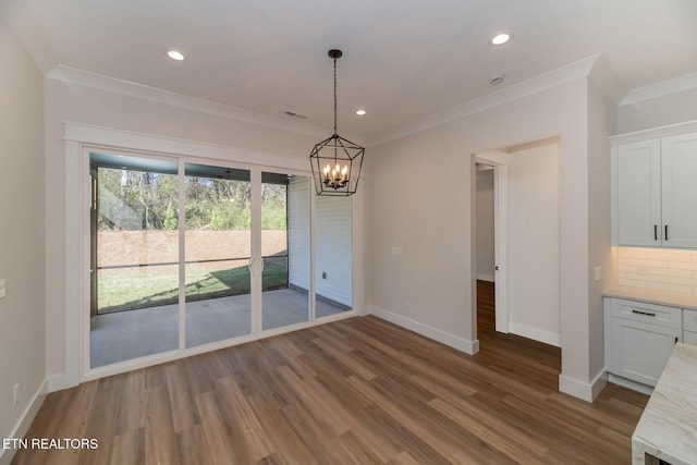 unfurnished dining area featuring dark wood-type flooring, crown molding, and a chandelier