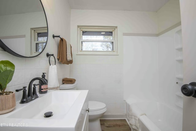 full bathroom with hardwood / wood-style flooring, tile walls, vanity, shower / bathtub combination, and toilet