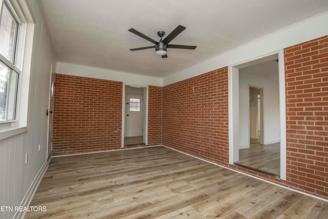 spare room featuring ceiling fan, brick wall, and light hardwood / wood-style flooring