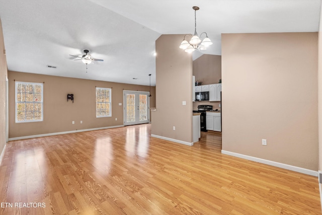 unfurnished living room with light wood-type flooring, ceiling fan with notable chandelier, vaulted ceiling, and a wealth of natural light