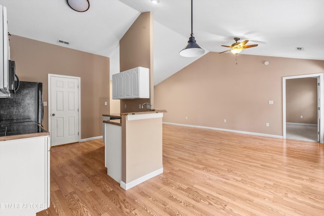 kitchen featuring kitchen peninsula, pendant lighting, vaulted ceiling, white cabinets, and light wood-type flooring