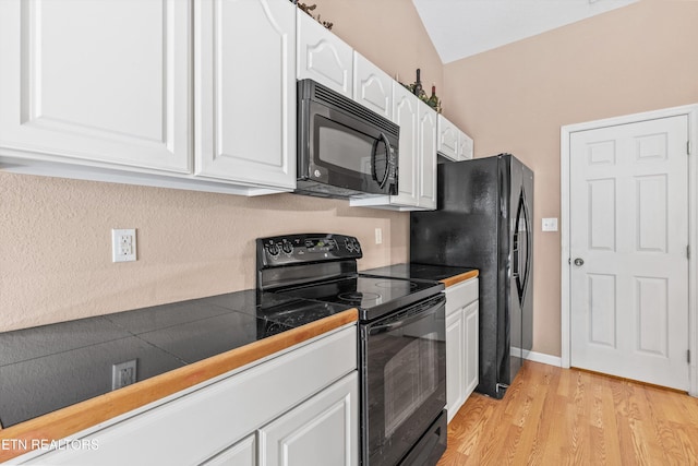 kitchen with light hardwood / wood-style floors, white cabinets, black appliances, and vaulted ceiling