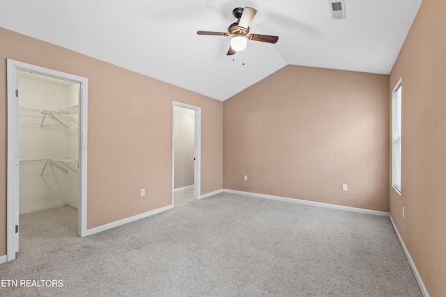 unfurnished bedroom with a walk in closet, light carpet, a closet, ceiling fan, and lofted ceiling