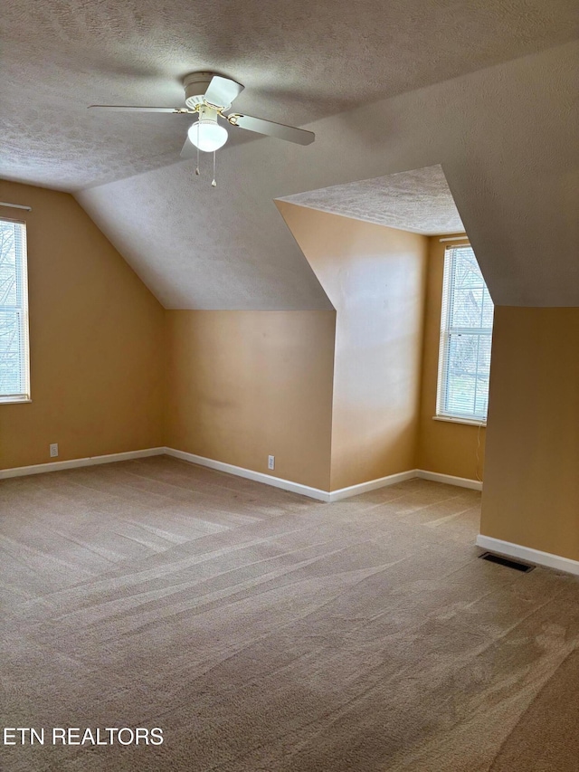 bonus room featuring ceiling fan, lofted ceiling, light carpet, and a textured ceiling