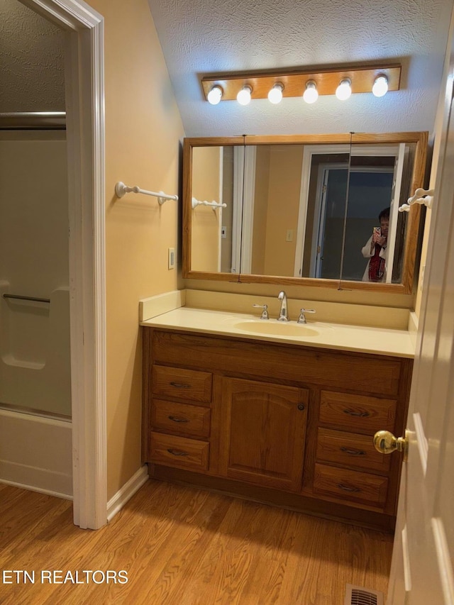 bathroom featuring vanity, bath / shower combo with glass door, hardwood / wood-style floors, and a textured ceiling