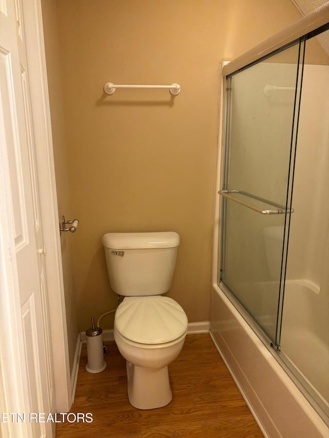 bathroom featuring hardwood / wood-style floors, toilet, and combined bath / shower with glass door