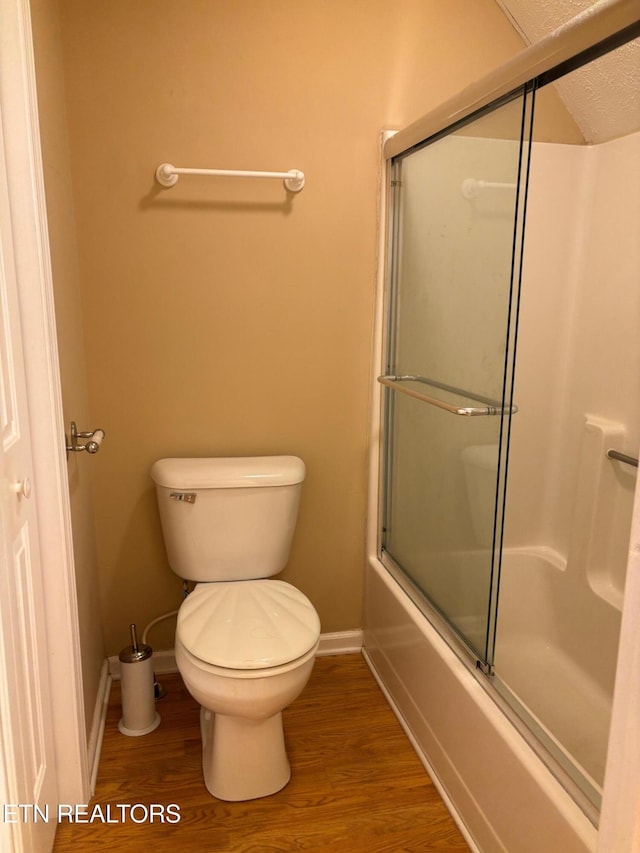 bathroom featuring a textured ceiling, wood-type flooring, toilet, and combined bath / shower with glass door