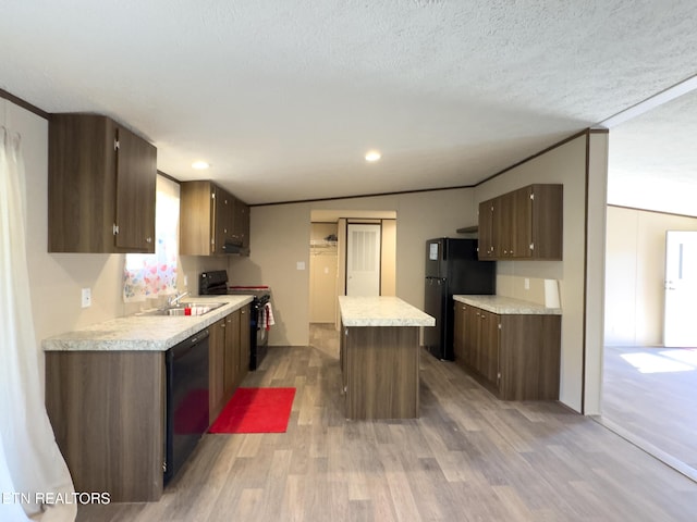 kitchen featuring light wood finished floors, a center island, light countertops, a textured ceiling, and black appliances