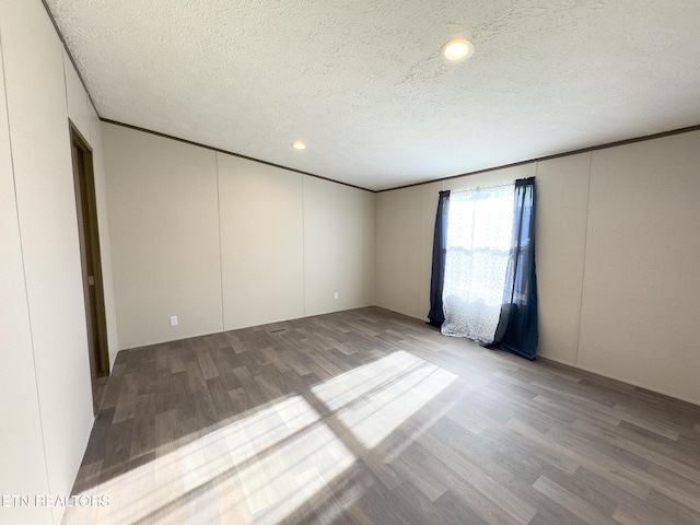 empty room featuring a textured ceiling, wood finished floors, and ornamental molding