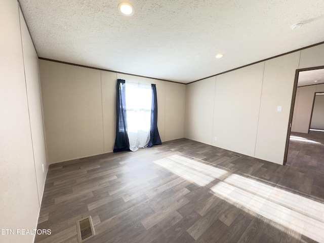 empty room featuring visible vents, a textured ceiling, wood finished floors, and ornamental molding