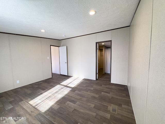 spare room with a textured ceiling, visible vents, dark wood-style flooring, and ornamental molding