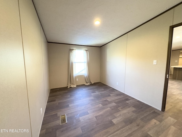 empty room with visible vents, a textured ceiling, wood finished floors, and crown molding