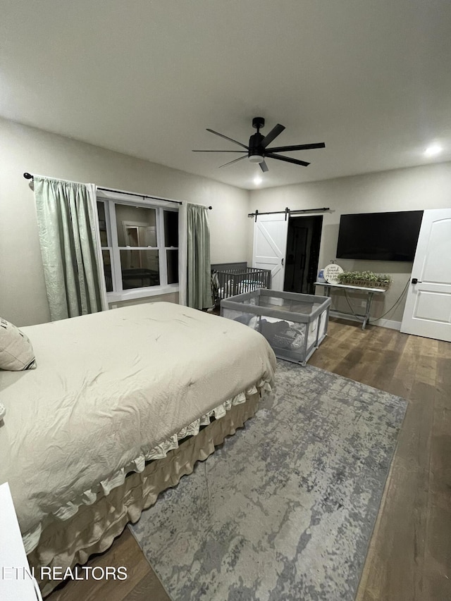 bedroom featuring dark hardwood / wood-style floors, ceiling fan, and a barn door