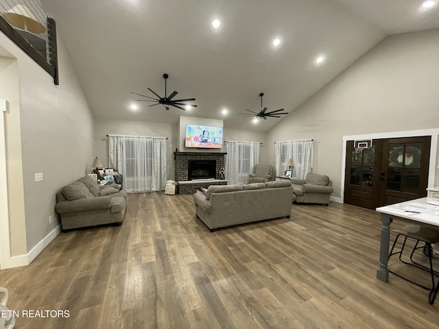 living room featuring hardwood / wood-style flooring, ceiling fan, high vaulted ceiling, and a brick fireplace