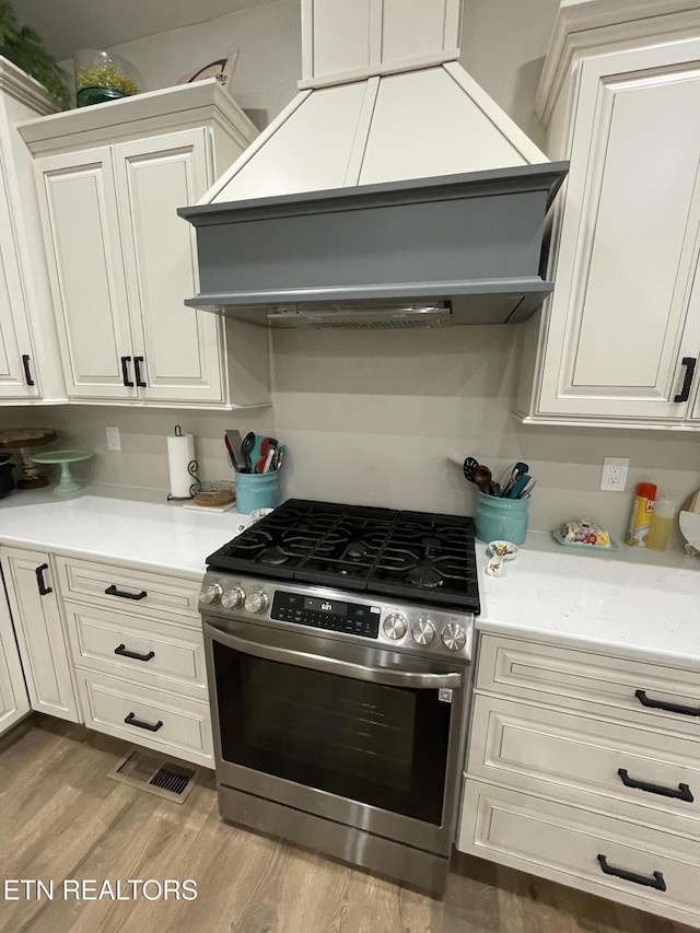 kitchen with white cabinetry, premium range hood, stainless steel range with gas cooktop, and light hardwood / wood-style flooring