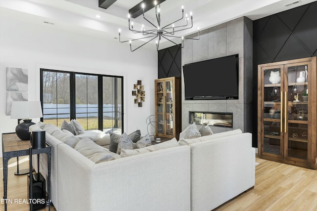 living room featuring light hardwood / wood-style flooring, beam ceiling, a chandelier, and a fireplace