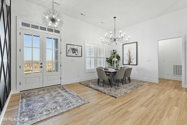 dining space with light hardwood / wood-style floors, french doors, and an inviting chandelier