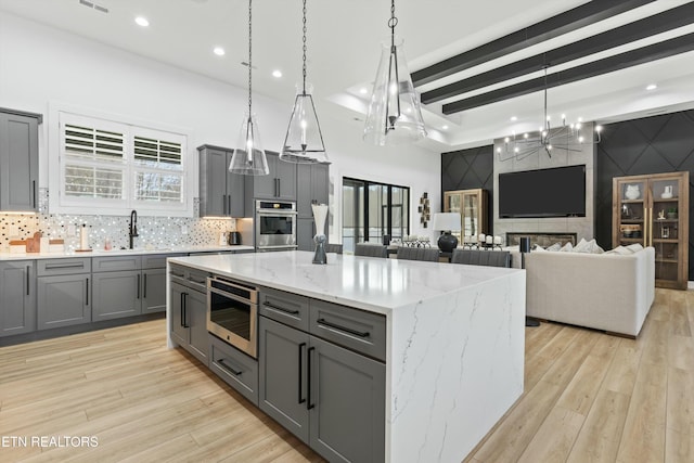 kitchen with light stone countertops, a large island, sink, decorative light fixtures, and gray cabinets