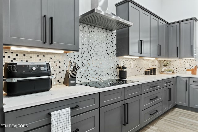 kitchen with wall chimney exhaust hood, gray cabinets, backsplash, and black electric stovetop