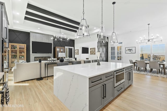 kitchen with a spacious island, appliances with stainless steel finishes, decorative light fixtures, light stone countertops, and gray cabinets