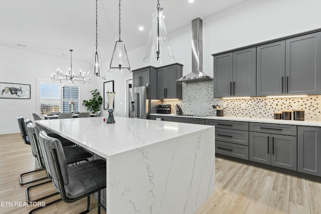 kitchen featuring a spacious island, wall chimney exhaust hood, decorative light fixtures, gray cabinetry, and high end fridge