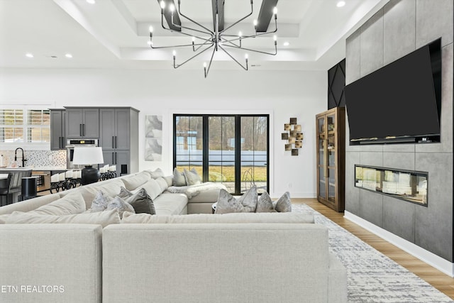 living room with light hardwood / wood-style floors, sink, a tray ceiling, and a tiled fireplace