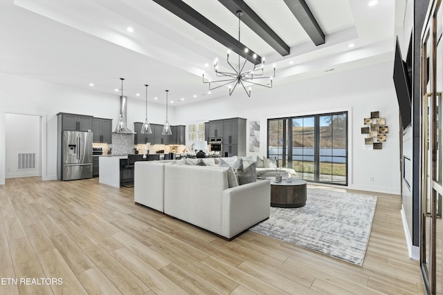 living room with a chandelier, a towering ceiling, light hardwood / wood-style flooring, and beam ceiling