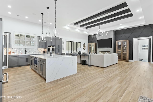 kitchen with light hardwood / wood-style floors, light stone countertops, hanging light fixtures, a large island with sink, and gray cabinets