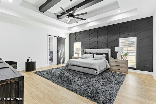 bedroom with light wood-type flooring, ceiling fan, a barn door, and a tray ceiling